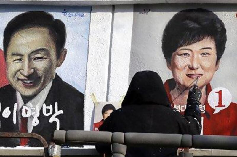 An artist paints the portraits of Lee Myung-bak, left, and his successor Park Geun-hye in Seoul last week. Lee Jin-man / AP Photo