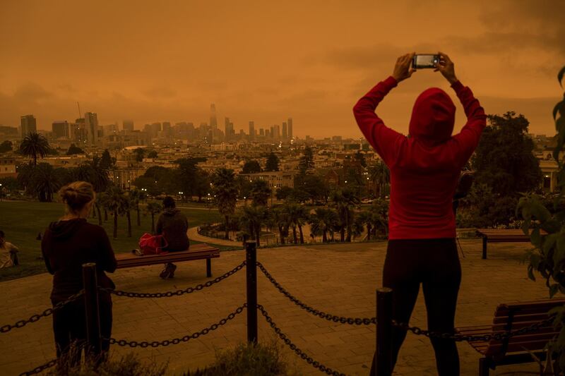 A person uses a mobile phone to take a photograph of smoke hanging over buildings in San Francisco, California, U.S. Bloomberg