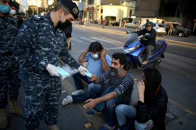 A Lebanese policeman, wearing a protective mask, distributes masks to protesters during a demonstration in the capital Beirut.   AFP