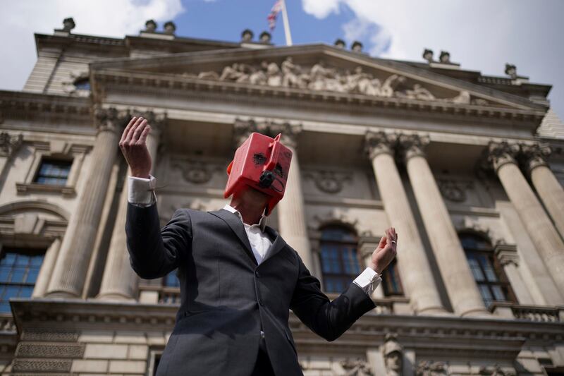 A man wearing a petrol can as a face mask speaks from the top of a barrel as climate activists from Extinction Rebellion hold a protest outside the offices of HM Revenue and Customs in Whitehall, central London. AP