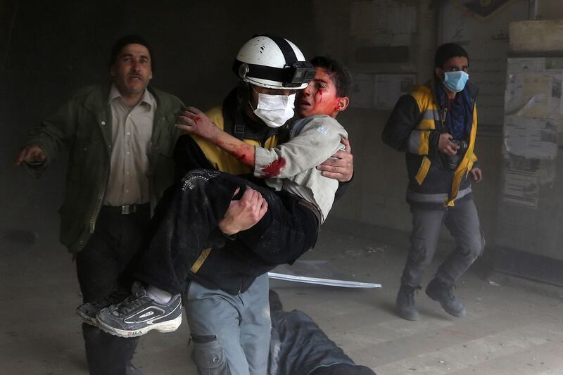 A member of the Syrian civil defence carries a wounded child from the rubble after a regime air strike in Jisreen on February 8, 2018. Abdulmonam Eassa / AFP