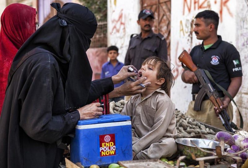A Pakistani health worker administers polio vaccine drops to a child, while a police security guard stands alert during a door-to-door vaccination campaign on the outskirts of Karachi on January 19, 2015. Asim Hafeez/The National