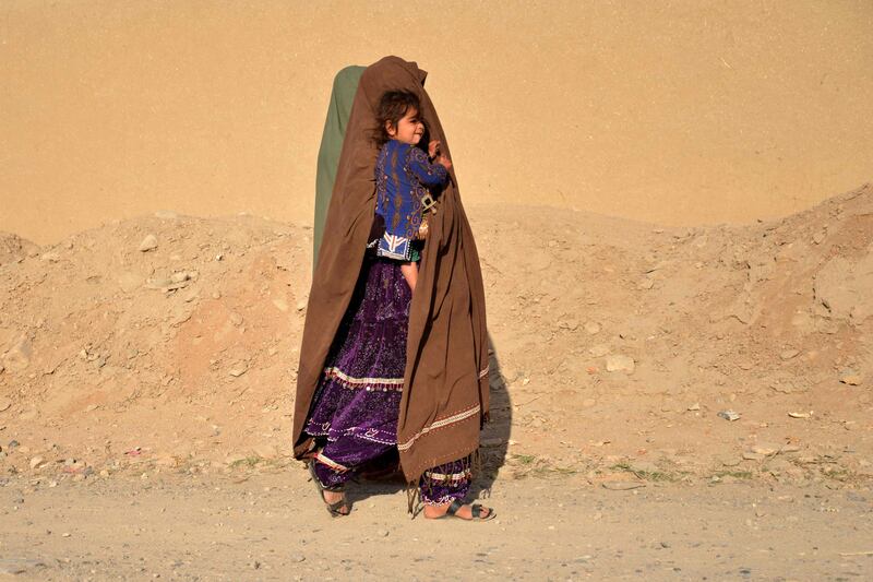 A woman carrying a child walks along a roadside in Kandahar province, Afghanistan. AFP