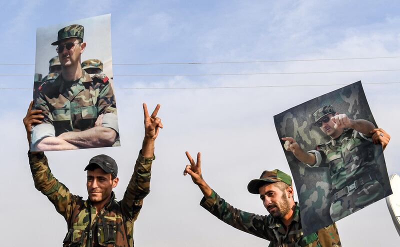 Syrian government soldiers hold up portraits of President Bashar al-Assad while flashing the victory gesture at a position on the outskirts of the northern city of Manbij in the north of Aleppo province as government forces deploy there.  AFP