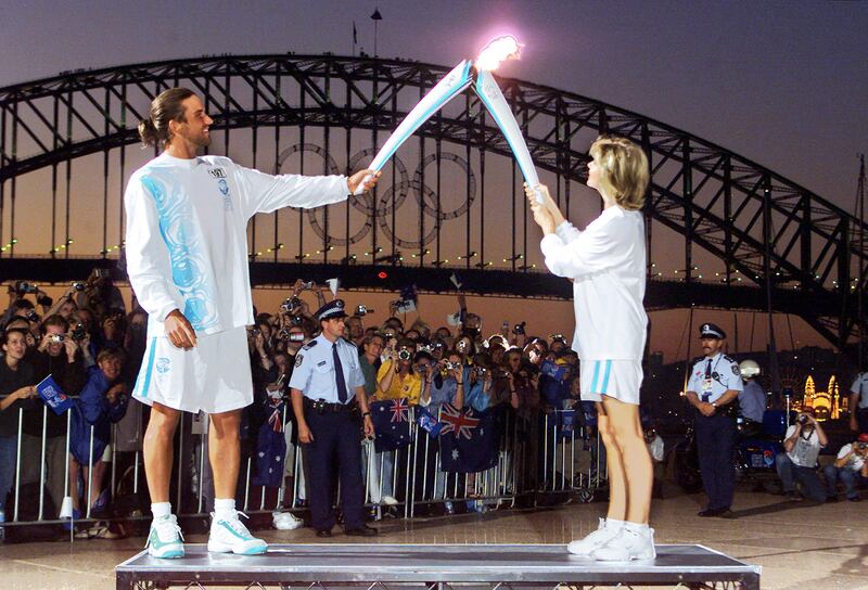 Newton-John passes the Olympic flame to Australian tennis player Pat Rafter in front of Sydney Harbour Bridge. AFP