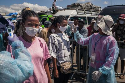 Ministry of Health staff measures passenger's temperature while several hundred people have gathered at the Maki bus station to take take buses to Madagascar's main cities, in Antananarivo, on April 7, 2020.  Despite the confinement of Antananarivo, the authorities allowed the population to move around Between April 7, 2020 and April 9, 2020, by taxi or plane. / AFP / RIJASOLO
