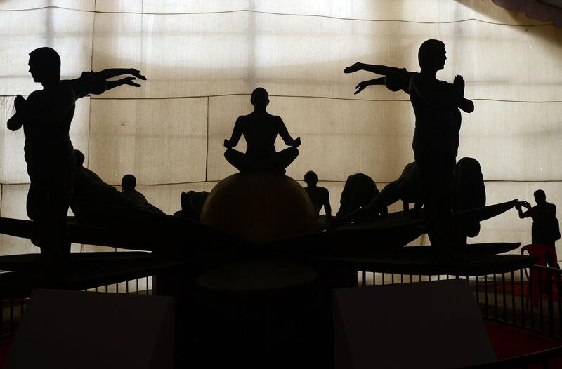 This picture shows the silhouettes of a visitor taking a photograph of a sculpture showing different yoga postures at North Central Zone Cultural Centre (NCZCC) in Allahabad. AFP