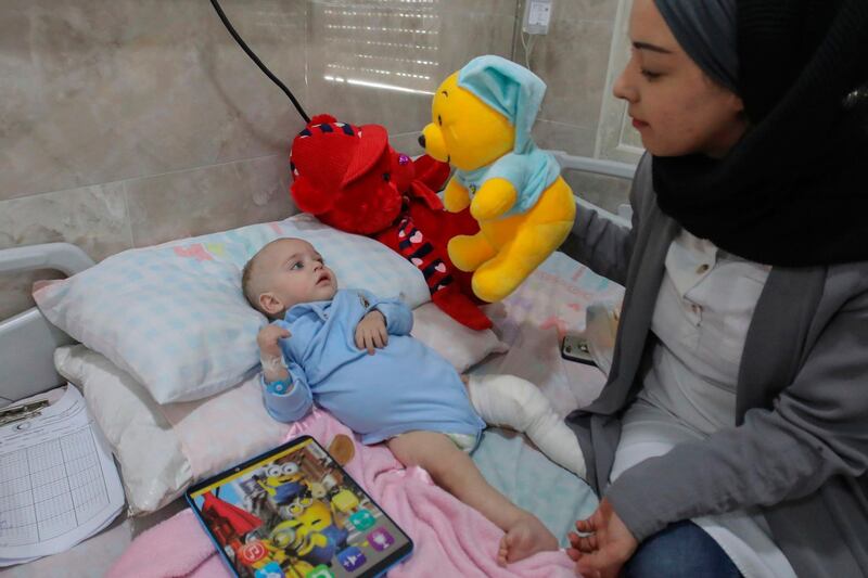 A volunteer plays with Mohammed Muheisen, a Palestinian baby from the Gaza Strip who is suffering from lung disease and a broken leg, at the Red Crescent Hospital in the West Bank town of Hebron. The nine-month-old baby was transferred from Gaza through Israel for treatment in September but is being cared for by volunteers after his mother was allegedly refused a permit to travel. AFP