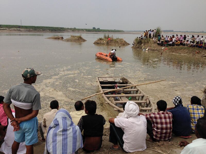 Rescuers search in the Yamuna River as villagers gather after a country boat, seen in foreground, capsized near Baghpat town in Uttar Pradesh state, India, Thursday, Sept.14, 2017. The boat crowded with construction workers capsized early Thursday and nineteen bodies have been pulled out of the river so far. (AP Photo/Altaf Qadri)