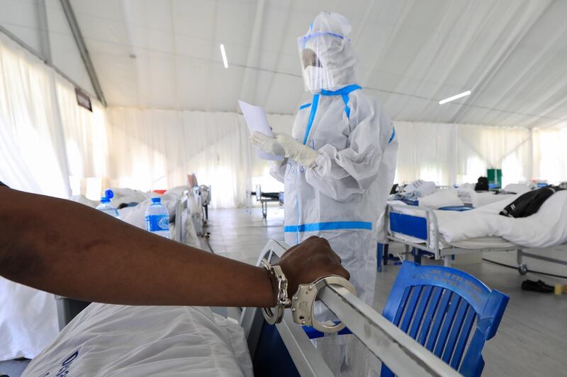 A Kenyan medical staff member checks the medical records of a Covid-19 patient and a prisoner while his hand is handcuffed on his bed in an isolation ward in Machakos, Kenya. EPA