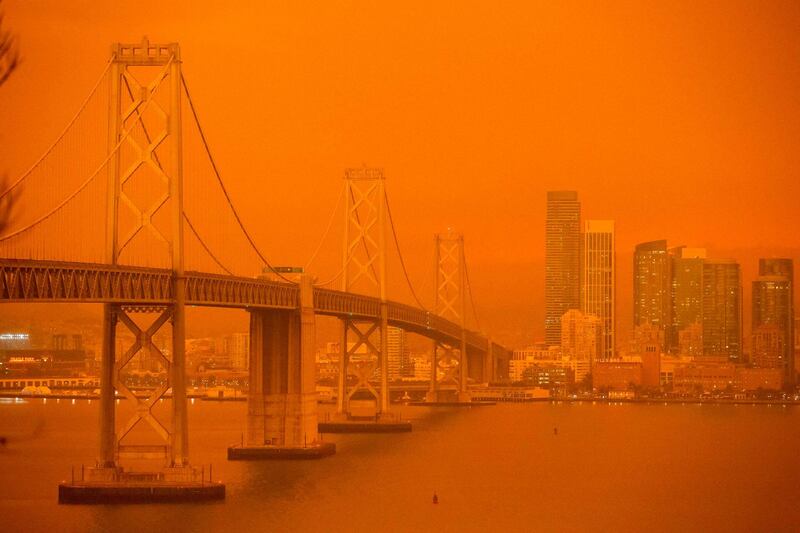The San Francisco Bay Bridge and city skyline are obscured in orange smoke and haze as their seen from Treasure Island in San Francisco, California.  AFP