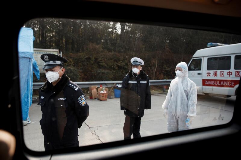 A medical worker in protective suit and police officers wait for drivers at a checkpoint in Yunxi county, Hunan province, near the border to Hubei province. Reuters