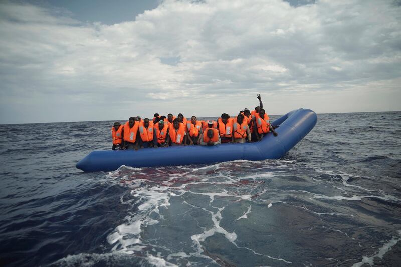 A migrant waves his hand in the air from on a blue rubber boat some 14 nautical miles from the coast of Libya in Mediterranean Sea, Sunday, Sept. 8, 2019. Humanitarian groups SOS Mediterranee and Doctors Without Borders have successfully rescued 50 migrants and brought them aboard the Ocean Viking. (AP Photo/Renata Brito)