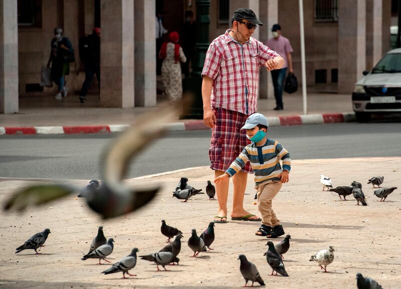 A mask-clad boy runs after pigeons near his father in the centre of Morocco's capital Rabat.   AFP