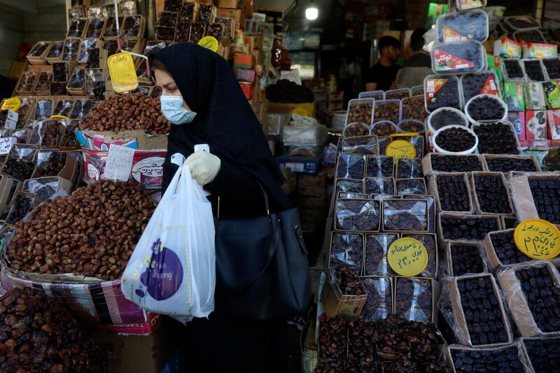 A woman wearing a protective face mask and gloves to help prevent the spread of the coronavirus carries her purchases as she leaves a store which sells dates, a favorite fruit for the Muslim holy fasting month of Ramadan, in southern Tehran, Iran. In Iran, the country that is hit worst in the Middle East by the coronavirus, all religious gathering, congregational prayers and communal Iftar servings, a meal eaten at sunset to break the fast, remain forbidden in the Ramadan and also holy shrines and religious centers also continue to be closed until at least May 4. AP
