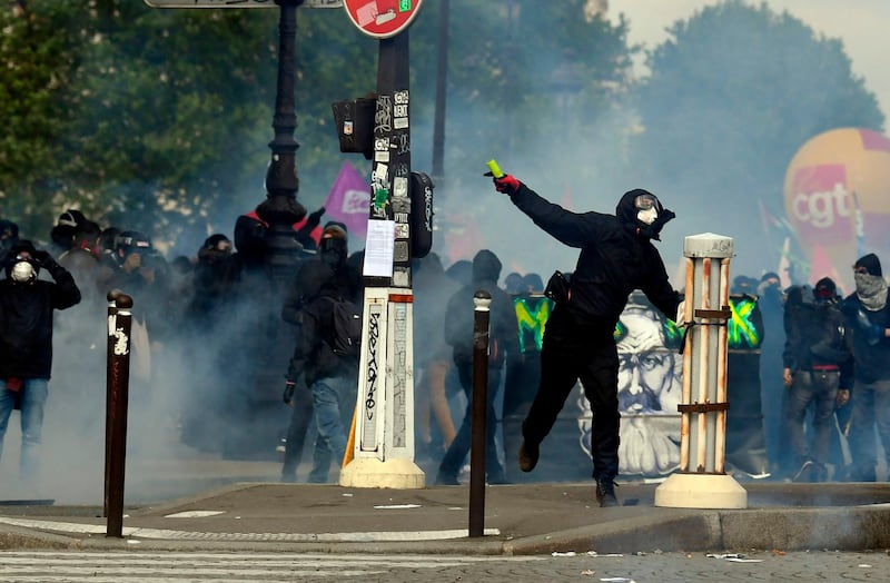 A protestor throws a missile towards police as teargas clouds rise. AFP/ALAIN JOCARD