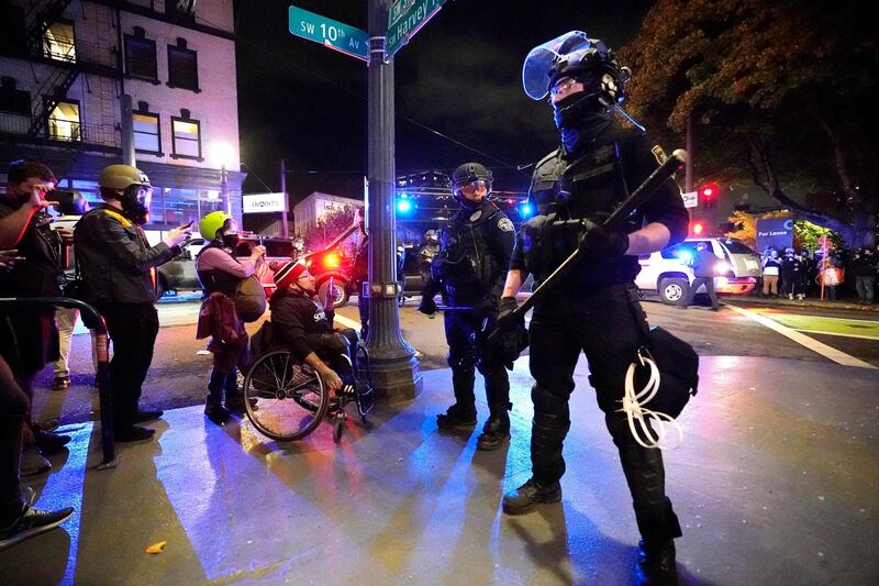 Police officers stand on a street corner near protesters, in Portland, Oregon. AP Photo