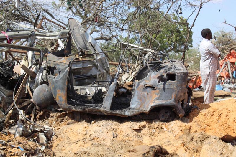 A man stands next to a destroyed vehicle at the scene of a large explosion near a check point in Mogadishu. EPA