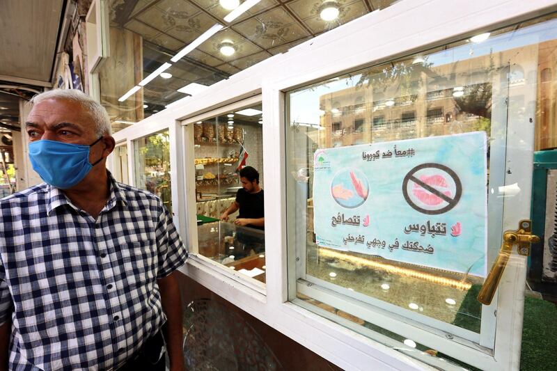 An Iraqi man wearing a protective face mask stands next to a sign reading in Arabic 'Together against Coronavirus, don't kiss, don't shake hands, your smile makes me happy' during the month of Ramadan, in Baghdad, Iraq. EPA