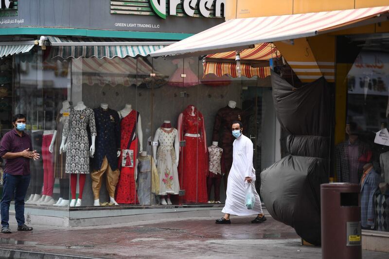 Men wearing surgical masks walk past and stand by closed shops in the Naif locality of the Gulf emirate of Dubai, on April 15, 2020, during a lockdown due to the COVID-19 coronavirus pandemic.  / AFP / KARIM SAHIB
