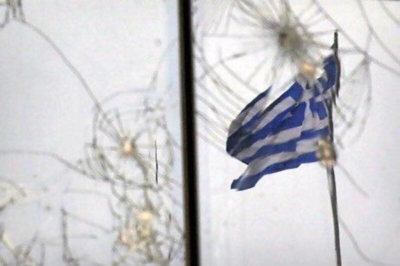 A Greek flag is seen through glass broken during previous protests in Athens. AFP