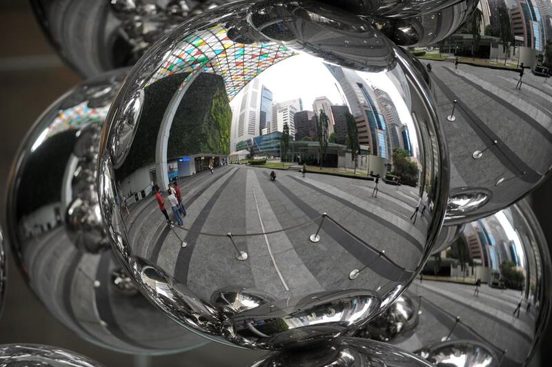 Financial district buildings are reflected on a metal ball sculpture in Singapore. Singapore's economic growth slowed sharply in the first three months of the year, data showed, but the central bank stood pat on monetary policy saying it would be lifted by a pick-up in global growth. ROSLAN RAHMAN / AFP