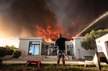 A man uses a garden hose to drench his house as a wild fire burns in the background, in La Couronne, near Marseille, on August 4, 2020. Several fires were raging on August 4 evening near Marseille, with one particularly fuelled by strong winds, ravaging nearly 300 hectares of vegetation in a coastal area of Martigues, according to the authorities. / AFP / Xavier LEOTY