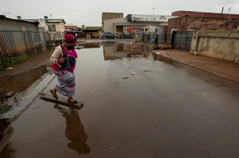 A woman wearing a mask crosses a waterlogged street after rainfall in Thokoza, east of Johannesburg, South Africa. AP Photo