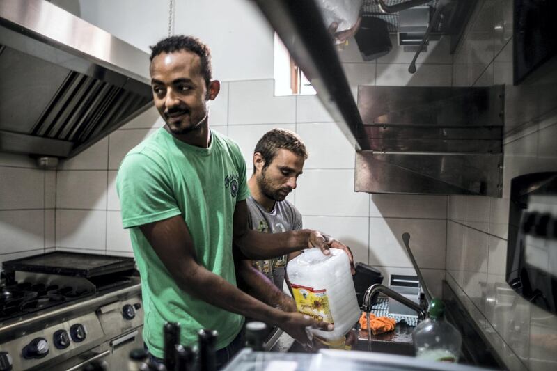 Two migrants hosted by a local association help to clean the kitchen before attending one of the cooking sessions. The National/Giacomo Sini