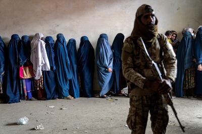 A Taliban fighter stands guard as women wait to receive food rations in Kabul. AP