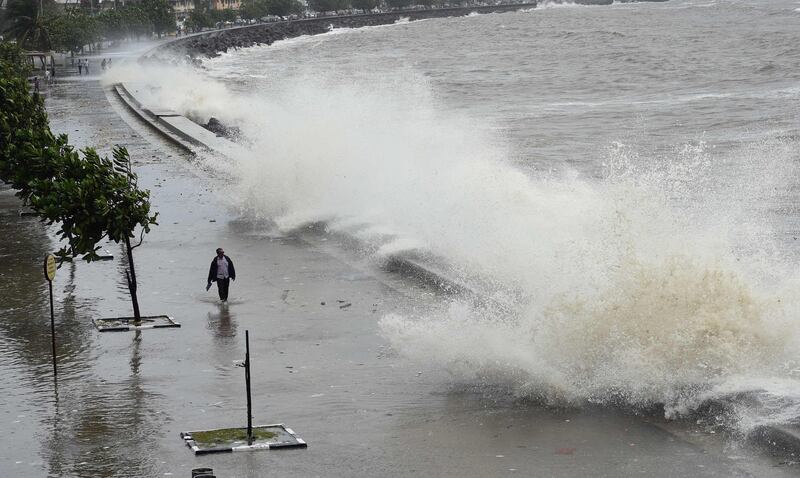 A man walks past as waves strike the promenade during high-tide in Mumbai on July 16, 2018.   / AFP / Indranil MUKHERJEE
