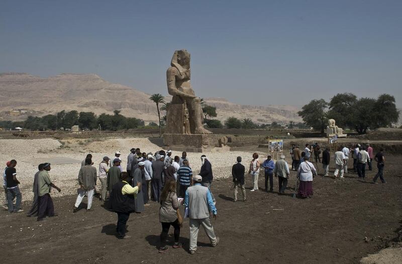 Tourists and journalists walk past a newly displayed statue of pharaoh Amenhotep III. The two monoliths in red quartzite were raised at what European and Egyptian archaeologists said were their original sites in the funerary temple of the king, on the west bank of the Nile.