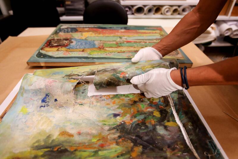 Gaby Maamary, a Lebanese artwork conservation specialist, examines a painting by late Lebanese artist Elie Kanaan, damaged in the Beirut port blast, at his studio in the capital Beirut. AFP
