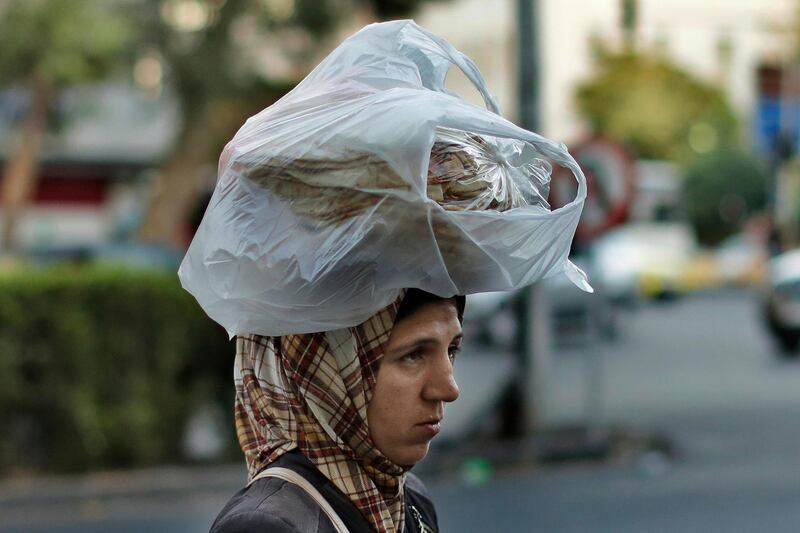 FILE - In this July 24, 2019 file photo, a woman carries bread on her head while she crosses a street in the Syrian capital, Damascus. In Syria nowadays, there is an impending fear that all doors are closing. After nearly a decade of war, the country is crumbling under the weight of years-long western sanctions, government corruption and infighting, a pandemic and an economic downslide made worse by the financial crisis in Lebanon, Syria's main link with the outside world. (AP Photo/Hassan Ammar, File)