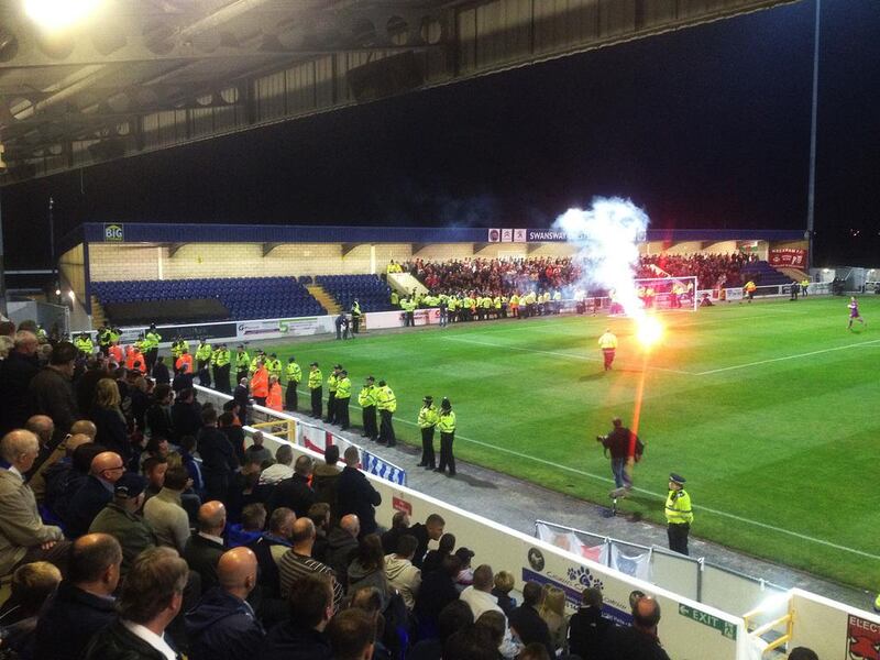 A view from the stands at Deva Stadium in Chester. Wrexham fans can be seen at the far end during the English Football Conference match againt old rivals Chester and Wrexham on Tuesday. A moment of silence to commemorate the 80th anniversary of a mining disaster that killed 266 was broken by a Chester fan shouting abuse, bringing outrage from the Wrexham fans present. A flare is thrown on the pitch as police line the touchline before the start of the match. Andy Mitten for The National



