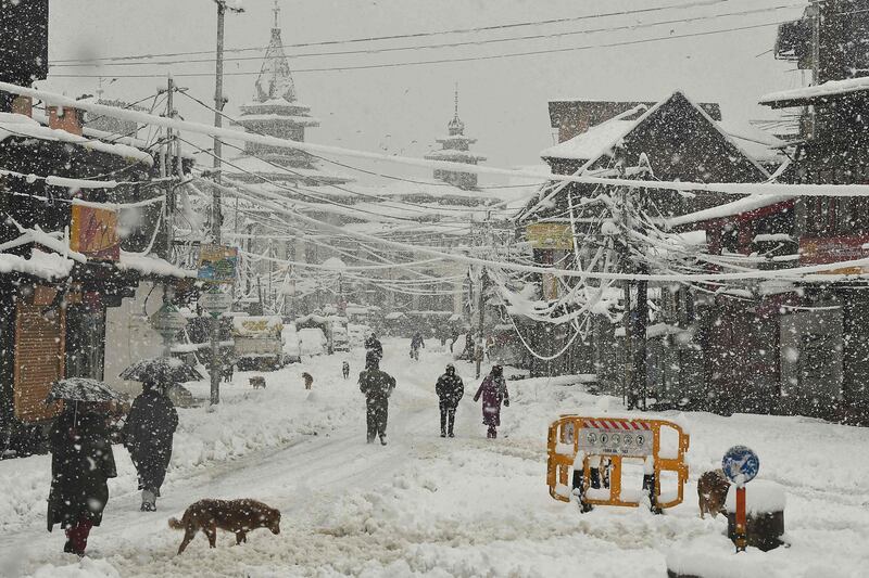 People walks along a road during a heavy snowfall in Srinagar on February 23, 2022.  (Photo by TAUSEEF MUSTAFA  /  AFP)