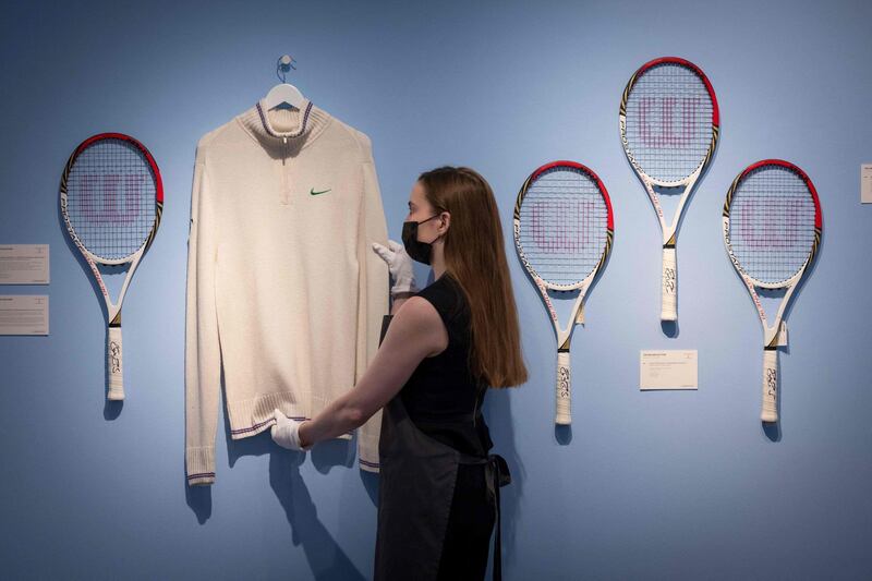 An assistant poses with Swiss tennis champion Roger Federer's cardigan and racket from Wimbledon 2012 (left) and rackets from the Olympics 2012 (right) during a photocall at Christie’s auction house in central London.