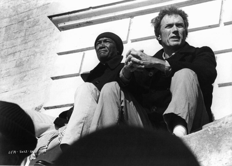Paul Benjamin and Clint Eastwood sitting on a cement slab next to each other in a scene from the film 'Escape From Alcatraz', 1979. (Photo by Paramount/Getty Images)