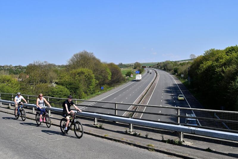 Cyclists ride bikes as the cross a bridge over empty carriageways of the M4 motorway below, near Swindon, western England, on April 11, 2020, as life in Britain continues over the Easter break, during the nationwide lockdown to combat the novel coronavirus pandemic. - Prime Minister Boris Johnson was able to walk in hospital on Friday some 24 hours after leaving intensive care treatment for COVID-19, as Britain recorded nearly 1,000 daily deaths from the virus for the first time. (Photo by JUSTIN TALLIS / AFP)