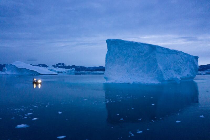 A boat navigates at night next to large icebergs in eastern Greenland.