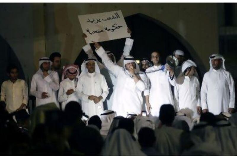 A Kuwaiti protester holds a banner reading "The people want an elected government" as another addresses fellow demonstrators outside the parliament building in Kuwait City late on June 10, 2011 during a rally demanding the resignation of the Gulf state's Prime Minister Sheikh Nasser Mohammed al-Ahmed al-Sabah.
