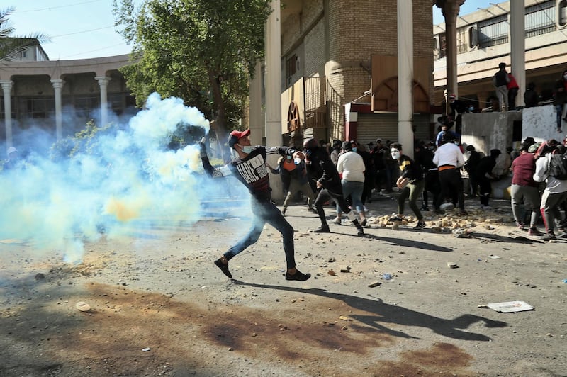 A protester throws back a tear gas canister fired by police during clashes in Baghdad, on Friday. AP Photo