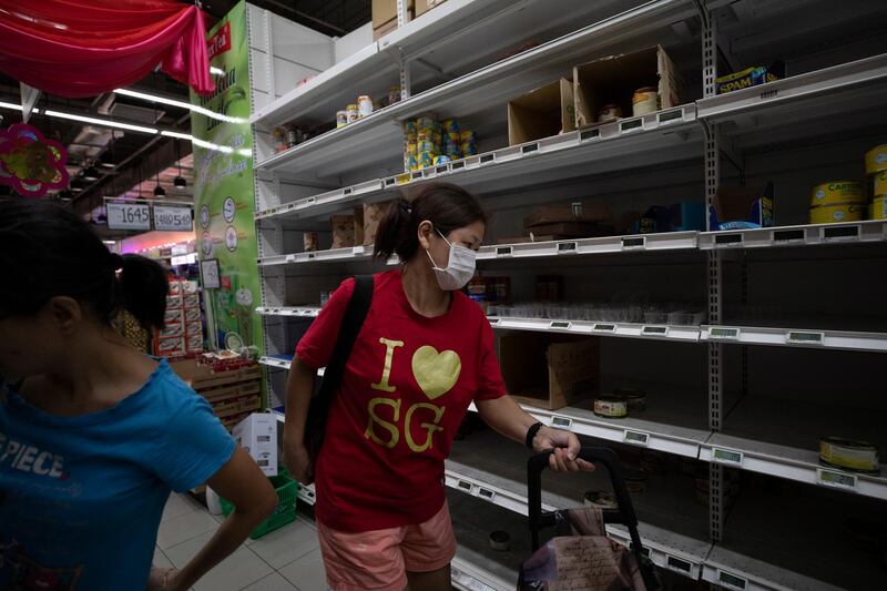 Customers walk by an almost empty shelf of canned food and instant noodles at a supermarket in Singapore.  EPA
