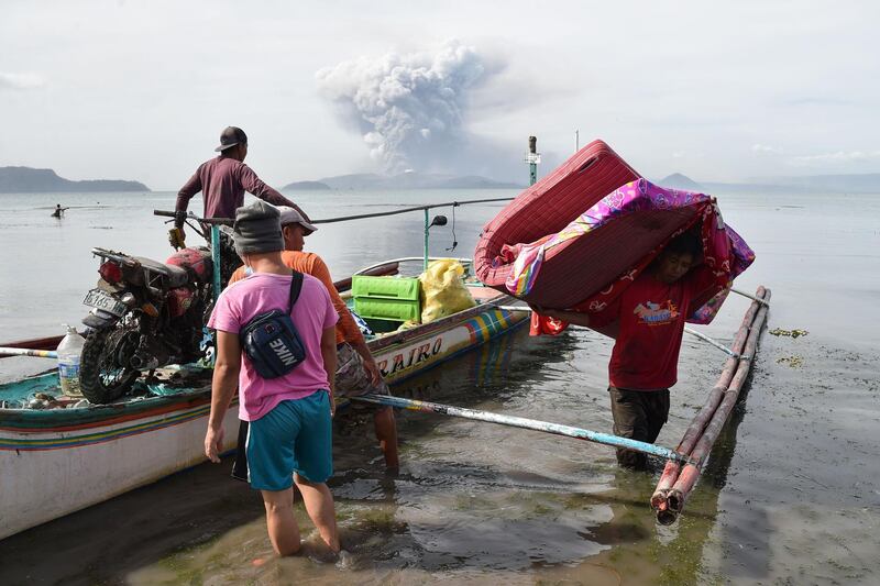 Evacuating residents living at the foot of Taal volcano unload their belongings from an outrigger canoe while the volcano spews ash as seen from Tanauan town in Batangas. AFP
