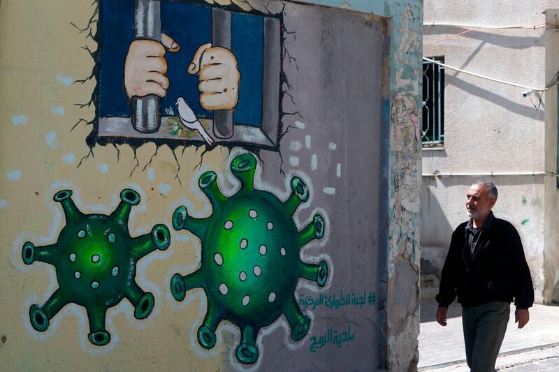 A Palestinian man walks past a mural depicting the coronavirus and a prison cell, in Gaza City. AFP