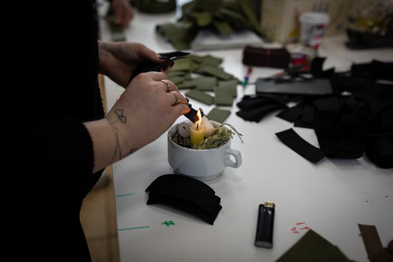 A woman securers the end of material for fastening vests by melting it over a candle in a makeshift factory in Mykolaiv.