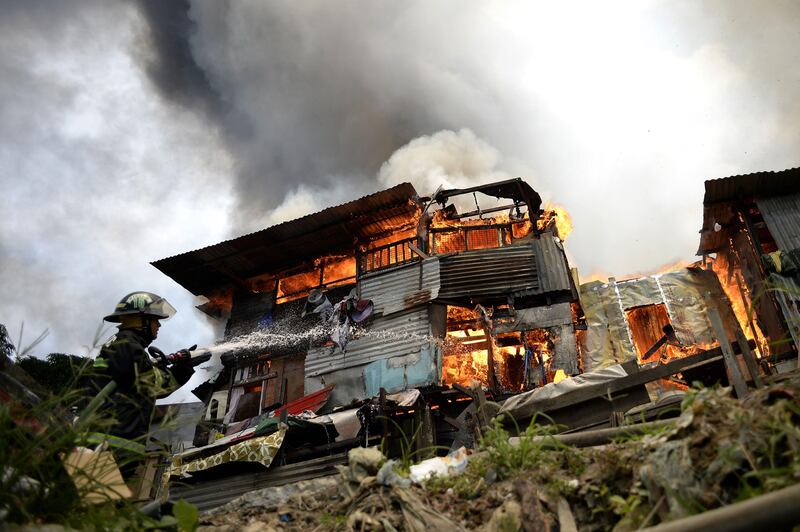A firefighter extinguishes flames as a fire engulfs an informal settlers area beside a river in Manila on August 11, 2017.
Fires are common hazards in the sprawling capital, where millions live in hovels made of scrap wood and cardboard and fire safety regulations are rarely imposed. / AFP PHOTO / NOEL CELIS
