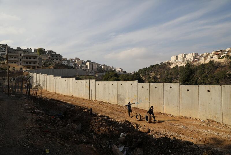 Children roll tires as they run along the Israeli barrier in the East Jerusalem refugee camp of Shuafat January 3, 2018. REUTERS/Ammar Awad