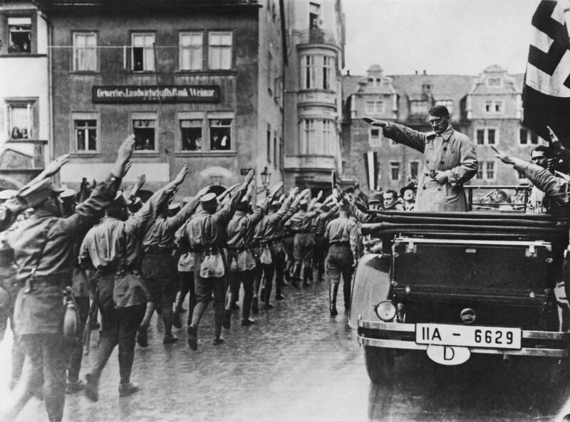 Nazi leader Adolf Hitler (1889 - 1945, in car, right) takes the salute as Sturmabteilung (SA) paramilitaries march past in the market square in Weimar, Germany, 13th November 1930. On the far right is Hitler's personal adjutant, Rudolf Hess (1894 - 1987). (Photo by Hulton Archive/Getty Images)