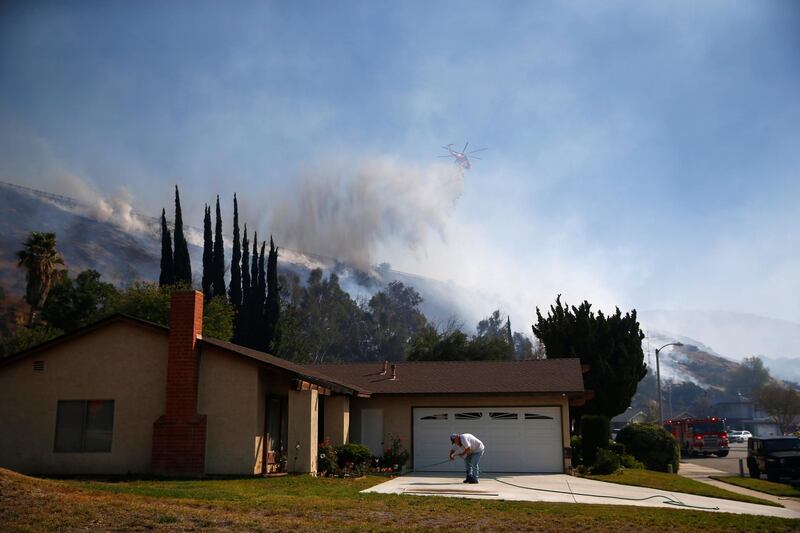 A resident connects a garden hose as firefighters battle the Peak Fire in Simi Valley. Reuters